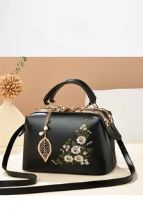 Close-up of delicate floral embroidery and leaf pendant on black leather handbag