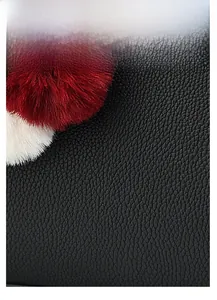 Macro shot of black crocodile texture faux leather with plush faux fur pom pom detail