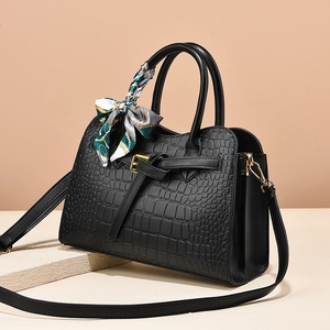 Elegant black crocodile-pattern handbag with silk scarf and gold hardware on stone base
