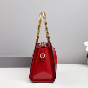Detail of red patent leather handbag featuring luxury gold woven handle and metal zipper