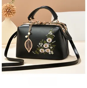 Detail of black pebbled leather handbag with daisy embroidery and gold pearl leaf pendant