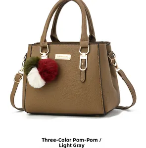 Detail of tan faux leather handbag featuring a colorful faux fur ball charm and gold hardware