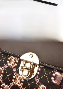 Detail of golden metal swivel lock on a dark brown textured leather crossbody bag