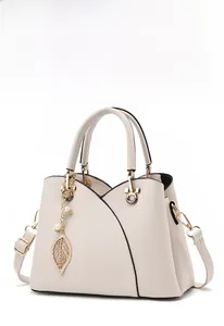 Detail of off-white lychee leather handbag featuring golden leaf pendant and pearl decor