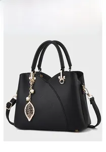 Detail of black lychee grain leather handbag with gold leaf charm and cross pleat design