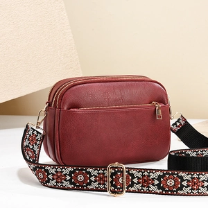 Burgundy faux leather crossbody bag with three zip compartments and patterned strap