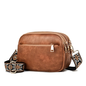 Brown leather crossbody bag with three zipper compartments and ethnic embroidered strap