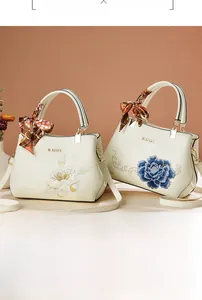 Detailed close-up of cream white handbag featuring exquisite floral embroidery and silk scarf handle