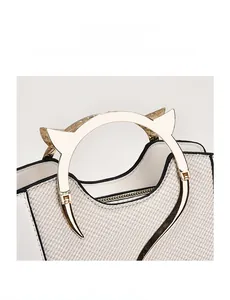 Close-up of cat-shaped gold metal handle and textured patchwork on white leather bag