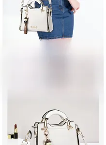 Detailed close-up of white leather handbag featuring gold metal handles and a cute cow charm