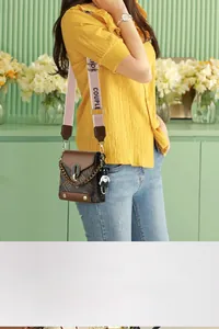Détail d'un sac bandoulière marron avec sangle rose et pendentif ours noir