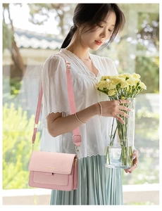 Pink canvas texture crossbody bag with a wide fabric strap shown in a sunny outdoor setting