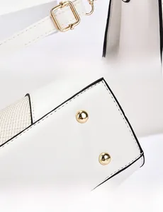 Detail of light gold hardware clasp and protective metal rivets on white leather bag