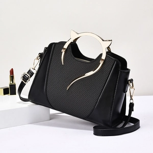 Elegant black shoulder bag with gold cat-ear handles and woven texture on geometric stand