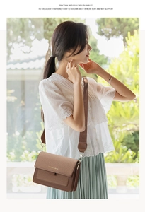 Detail view of brown crossbody bag with woven flap texture and wide fabric strap in garden setting