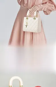 Detail of quilted beige handbag featuring gold ring handles and cross pendant charm