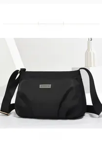 Front view of black nylon crossbody bag with metal logo plaque and adjustable strap