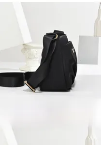 Side view of black nylon crossbody bag with wide strap and gold metal hardware detail