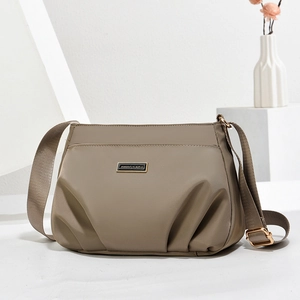Minimalist khaki nylon shoulder bag with adjustable strap on a modern white display base