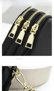Close-up of golden zippers and hardware on a multi-layer black nylon mini shoulder bag