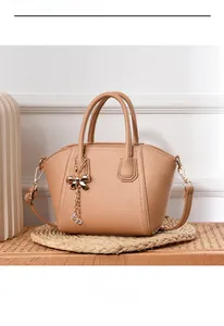 Detail of light brown lychee textured shell bag with golden bow tassel charm on wood