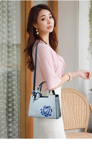 Sac à main bleu en cuir avec broderie florale et foulard porté par un mannequin