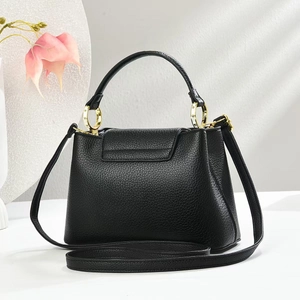 Detail der schwarzen Handtasche aus Narbenleder mit runden Griffen und goldener Hardware