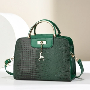 Dark green crocodile texture handbag with gold hardware and deer charm on white podium