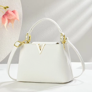 Detail der weißen Handtasche mit Litschimuster, goldenem V-Verschluss und Tragegriff