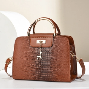 Detail of brown crocodile pattern handbag with golden metal handles and a deer charm