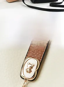 Dettaglio del rilievo dell'orso dorato su borsa in pelle avorio con finiture marroni