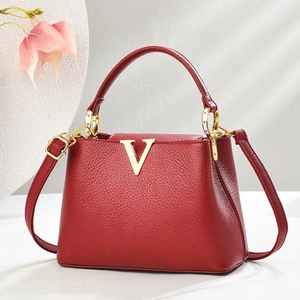 Detail der roten Tasche aus Litschileder mit goldenem V-Verschluss auf weißem Ständer