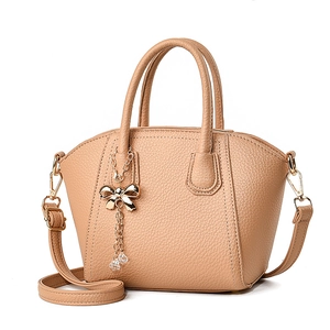 Elegant beige shell-shaped tote bag with golden bow pendant and crossbody strap