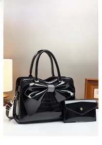 Detail der schwarzen Lackleder-Beuteltasche mit Krokoprägung, Schleife und passendem Etui