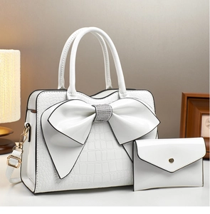 Detail der weißen Beuteltasche mit Krokoprägung, Strass-Schleife und passender Clutch