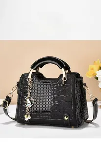 Detail of black crocodile embossed handbag with gold handle and pearl bunny pendant