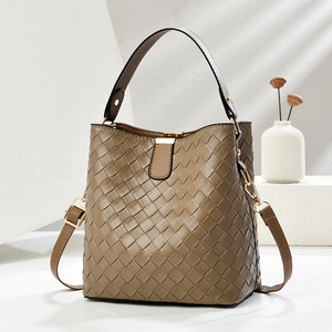 Brown woven bucket bag with leather handle and detachable strap in a minimalist setting