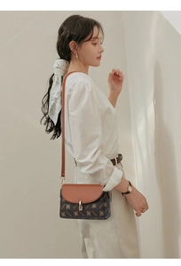 Detail of elegant two-tone crossbody bag with monogram pattern and gold buckle on a model
