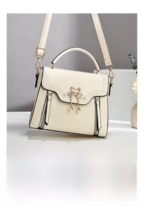 Close-up of cream crossbody bag featuring a golden twin swan buckle with pearls and crystals