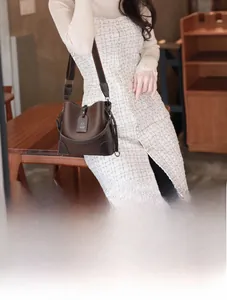 Detail of dark brown pebble leather bucket bag with wide canvas strap and metal charms