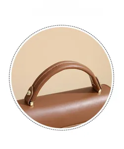 Dettaglio del manico tubolare e della ferramenta dorata su borsa in pelle marrone