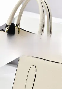 Close-up of beige lychee grain leather handbag featuring black edge paint and gold hardware