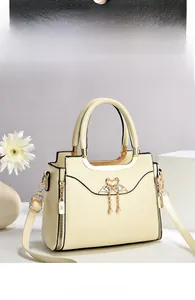 Detail of off-white tote bag featuring a gold swan buckle with rhinestones and pearls