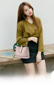 Detail of a pink bucket bag with woven texture and gold clasp held by a stylish model