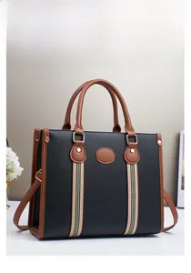 Detail of large black pebbled tote bag featuring brown handles and striped ribbon accents
