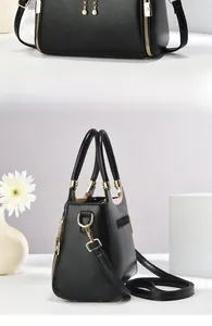 Detail of black tote bag with gold hardware and spherical zipper charm on a stand