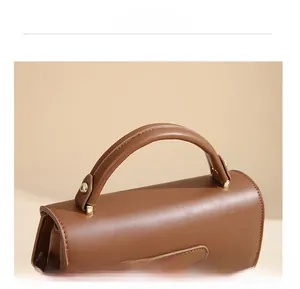 Dettaglio del manico in pelle marrone della borsa con finiture dorate e cuciture