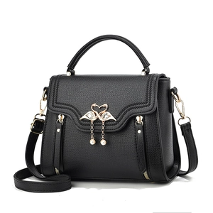 Minimalist black pebble leather top handle bag with gold swan pearl clasp and crossbody strap