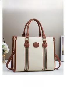 Detail of cream tote bag with litchi texture, striped webbing and brown leather handles