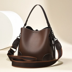 Chic dark brown leather bucket bag with a wide adjustable shoulder strap on a clean background